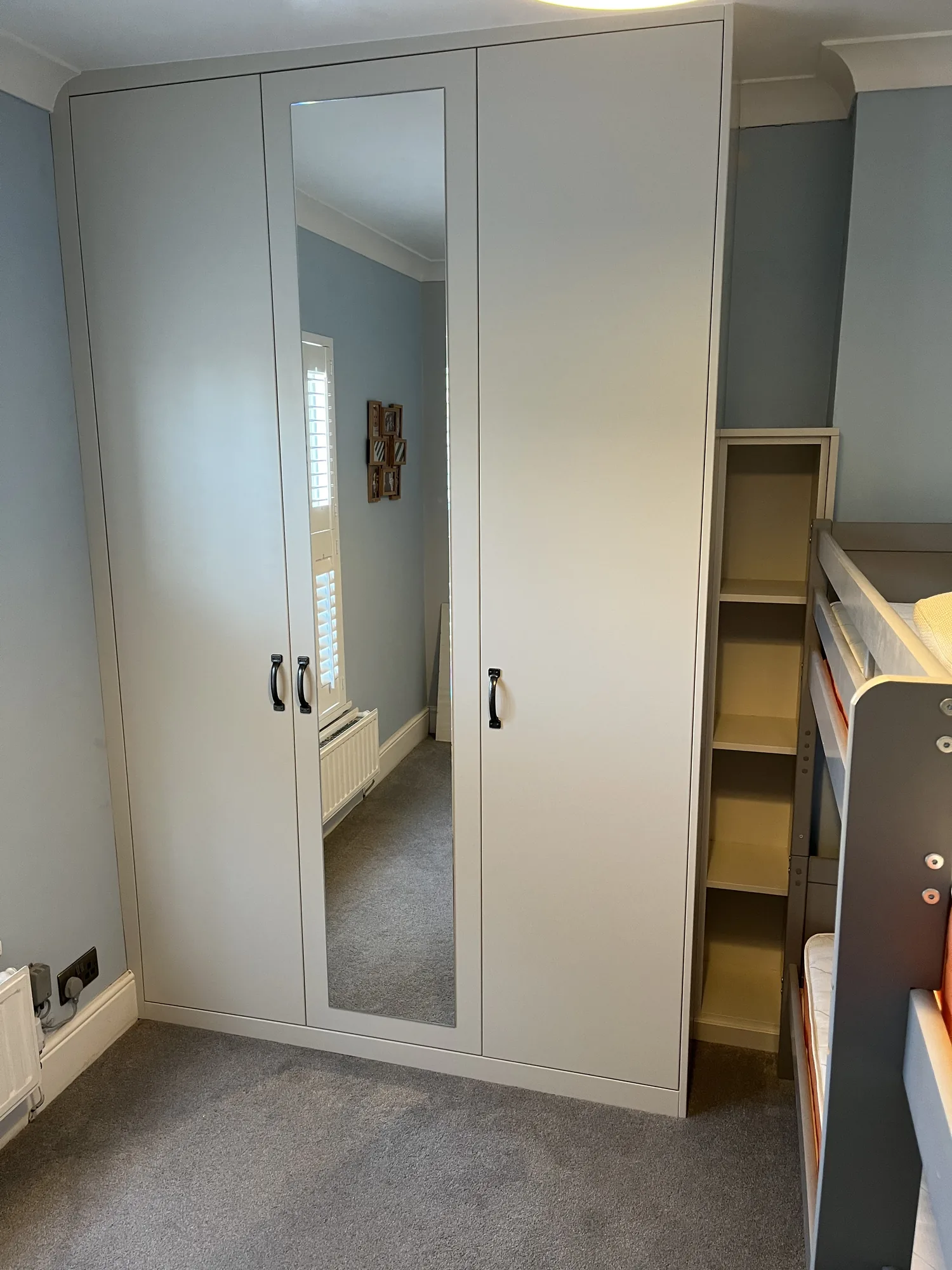 Three-door fitted wardrobe in a soft pale finish with side shelving